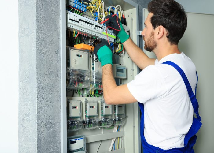 Electrician checking electric current with multimeter indoors
