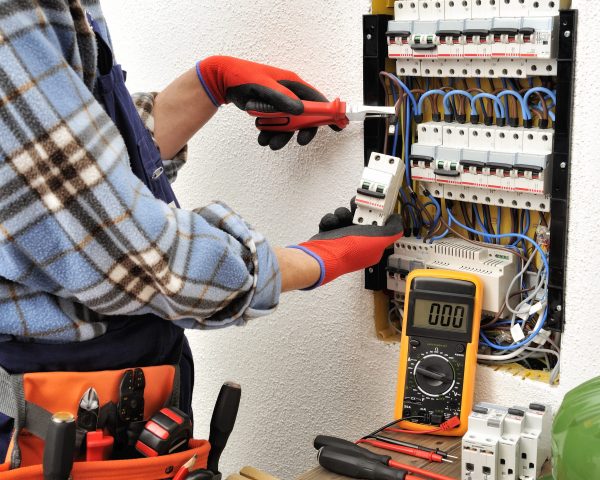 Young electrician technician introduces the electric cable into the clamp of the magnetothermic switch with an insulated clamp